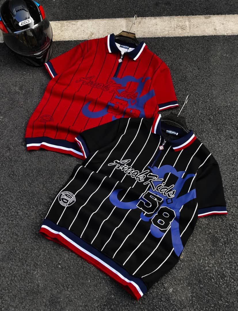 Red and black striped polo shirts with Amok Kids graphic prints and number 58 on asphalt next to a helmet.