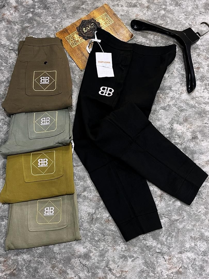Black ribbed joggers shown alongside folded olive, sage, mustard and green pairs highlighting logo embroidery.