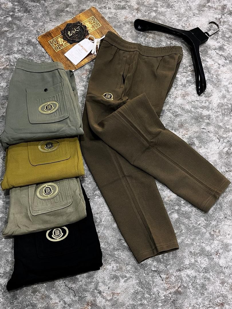 Olive green ribbed joggers displayed next to folded pairs in black, mustard, sage and light green showing embroidered details.