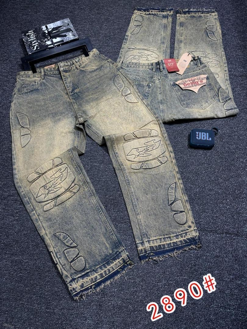 Light wash baggy jeans with embroidered designs on legs and back, flat lay with tags and JBL speaker.