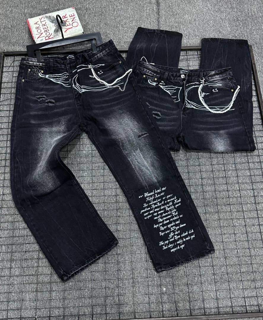 Black baggy jeans with white prints, chains, and text details shown in flat lay with front and back views.