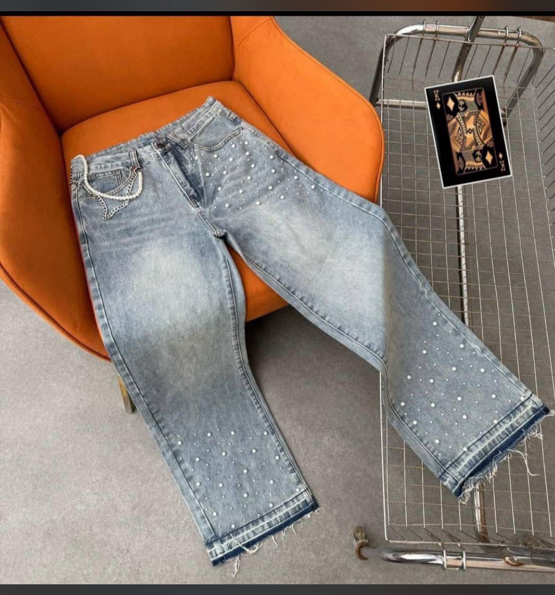 Light blue baggy jeans with pearl studs and chain on orange chair.