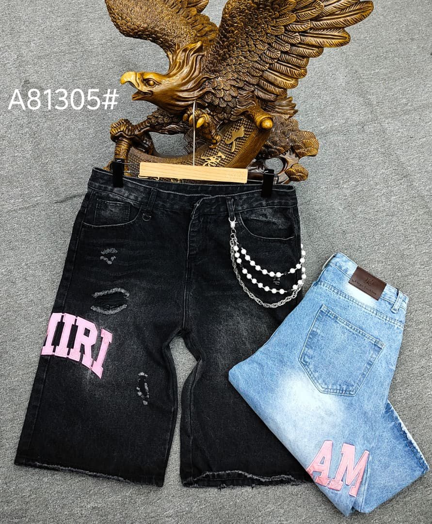 Black baggy AMIRI jorts on hanger with pink lettering, rips, and chain next to folded light blue pair.