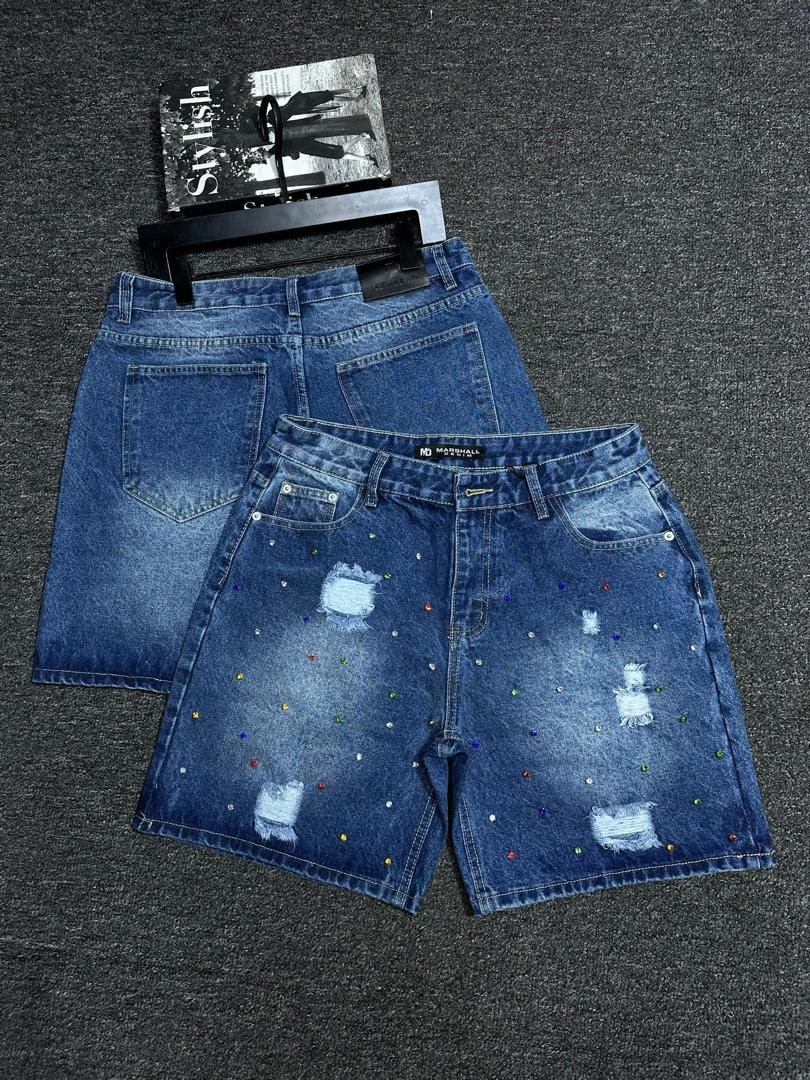 Blue baggy denim shorts with multicolored studs, rhinestones and distressed rips shown flat.