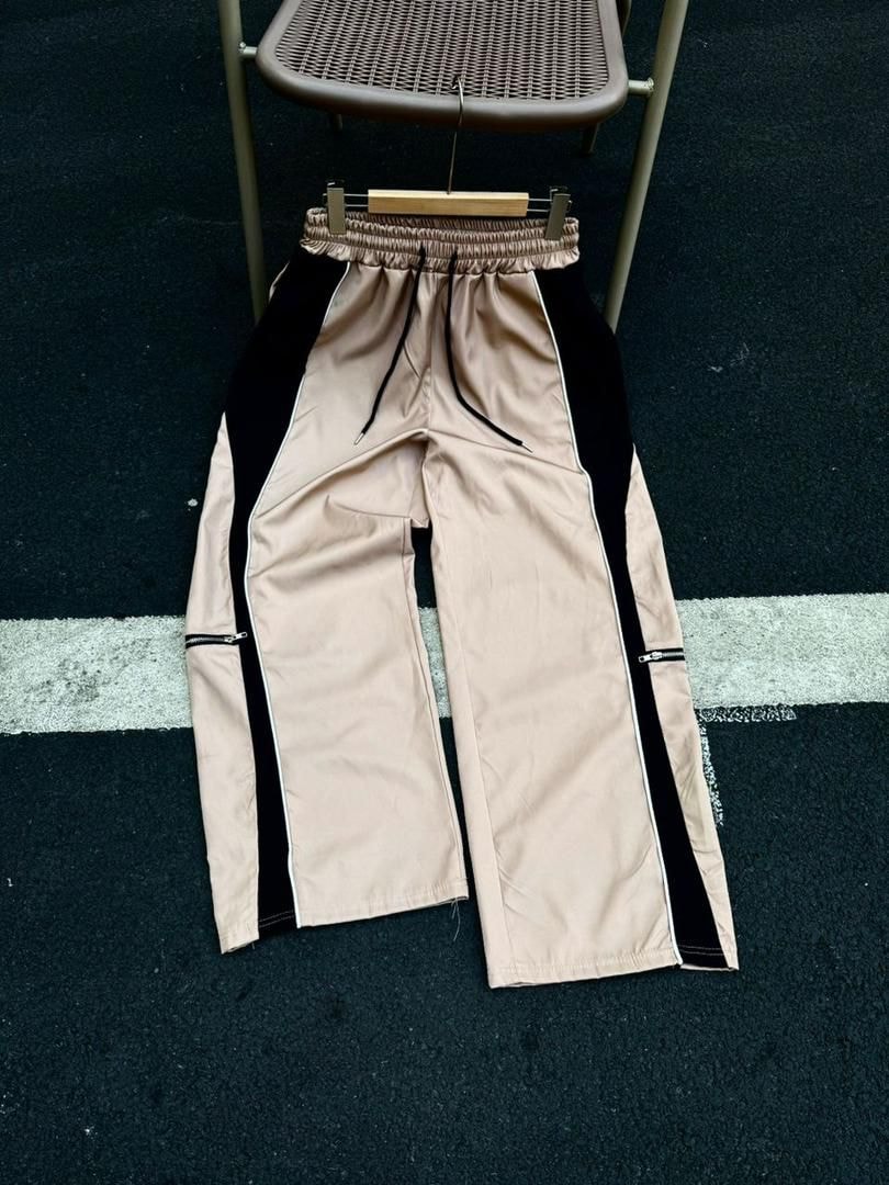 Beige colorblock joggers with black panels and side zips displayed flat.