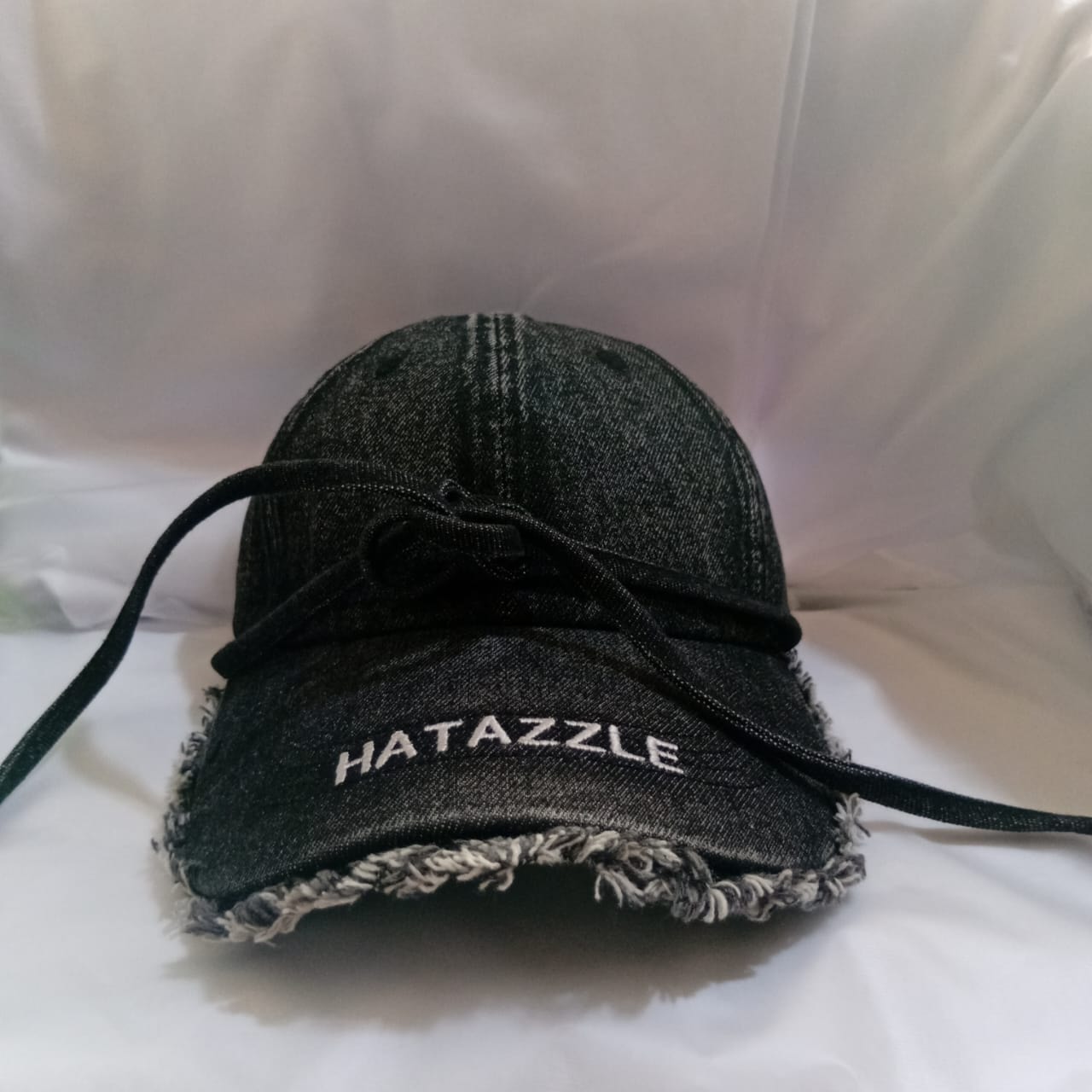 Black denim Hatazzle cap with tie strings and frayed brim.