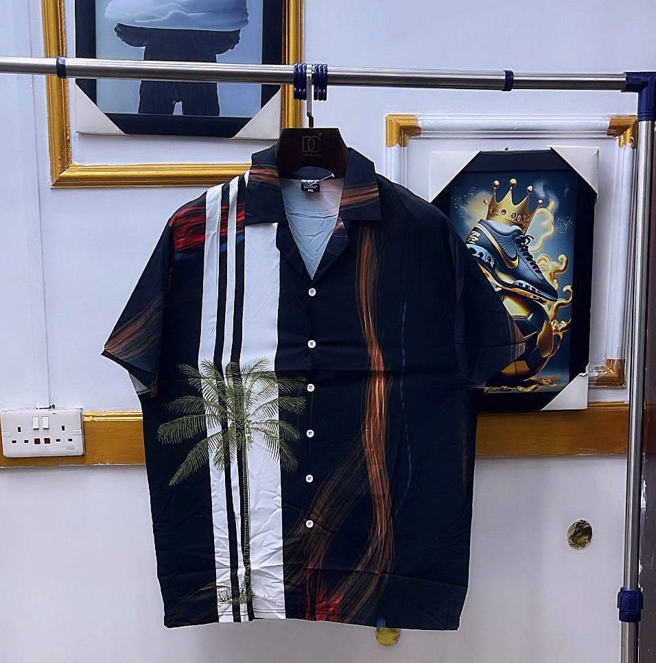 Black short sleeve shirt with white stripes, palm tree and colorful print hanging.