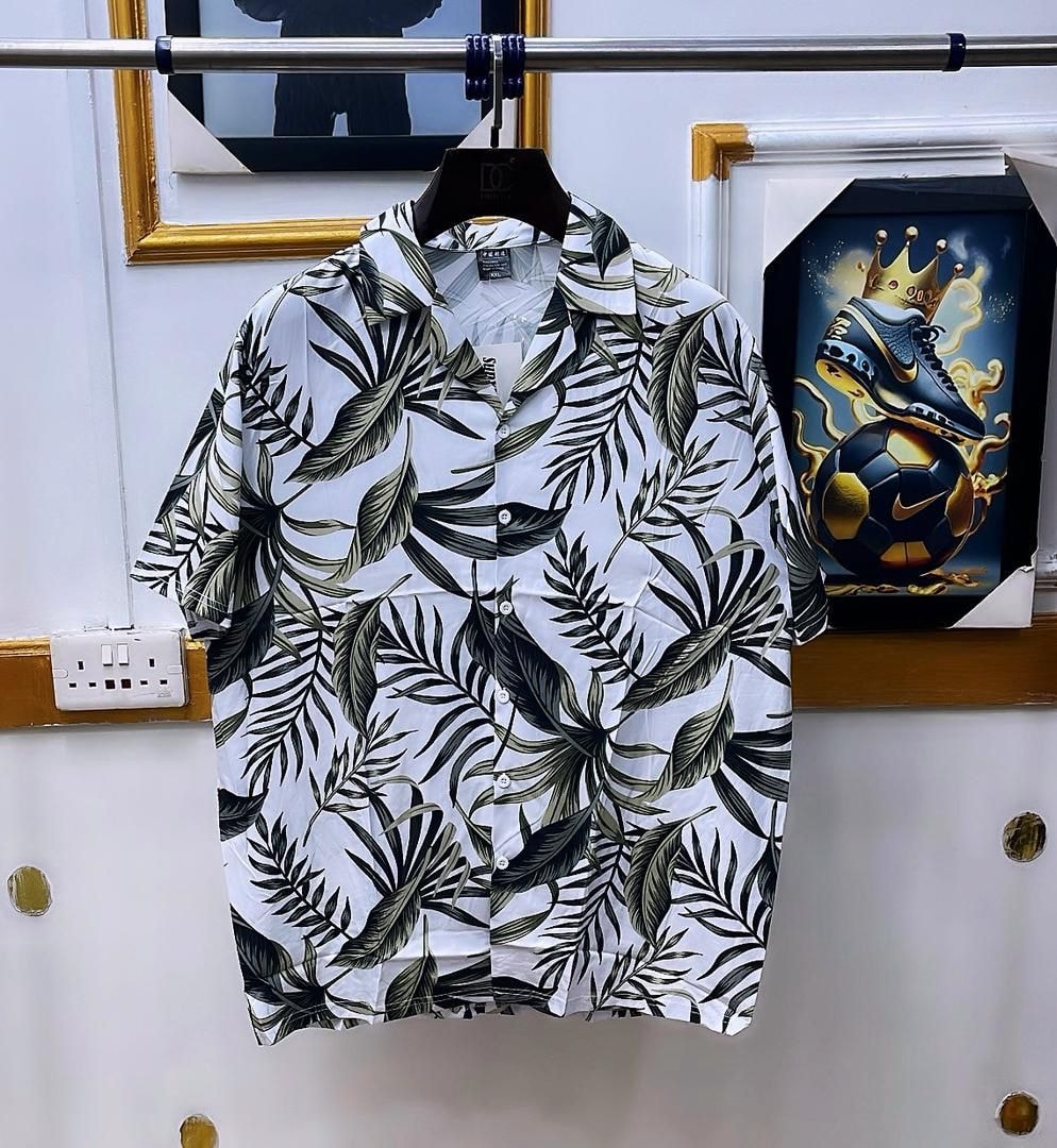 White short sleeve shirt with green leaf print hanging on metal rack.