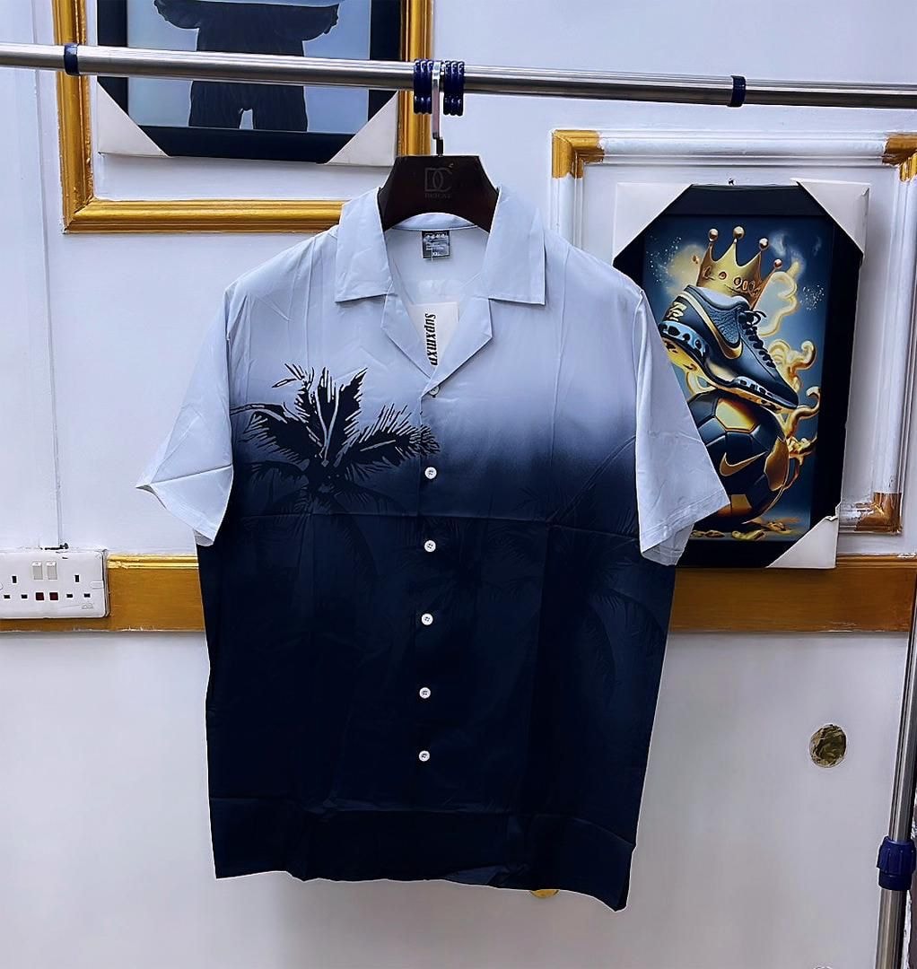 Blue gradient short sleeve shirt with palm tree print hanging on rack.