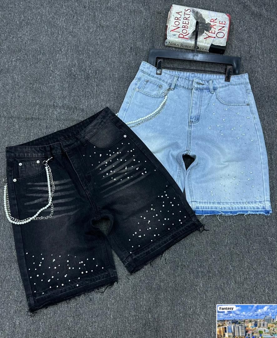 Black and light blue denim shorts with pearl rhinestone embellishments and chains on gray surface.