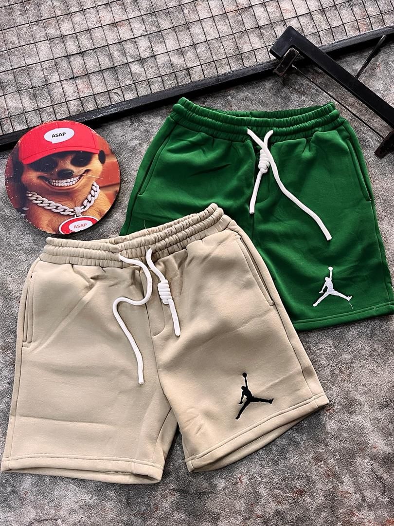 Green and beige fleece jogger shorts with Jumpman logo on textured surface.