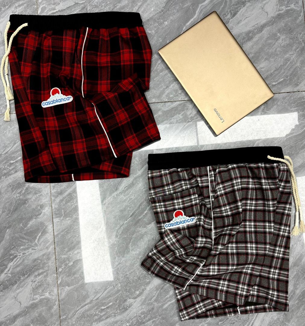 Red and black plaid Casablanca shorts with black waistband above grey plaid version on tiled floor.