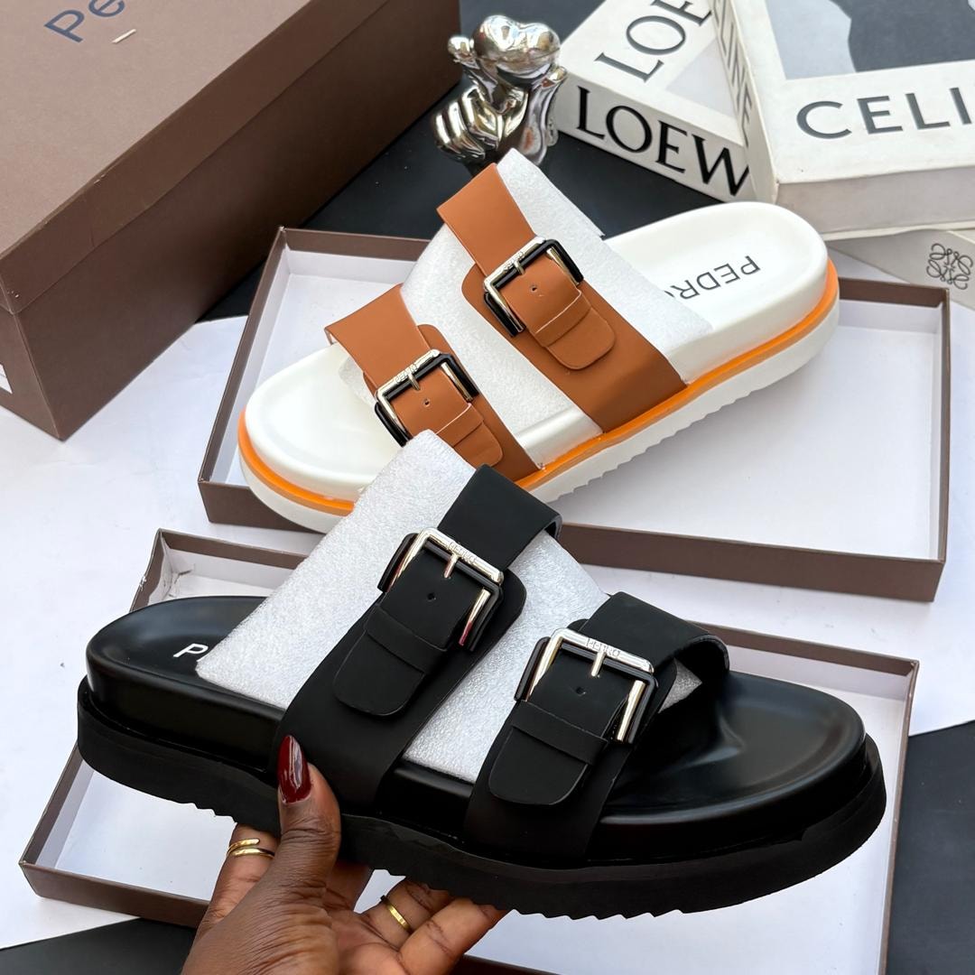 Brown and black PEDRO double buckle platform slides shown in boxes with branding.
