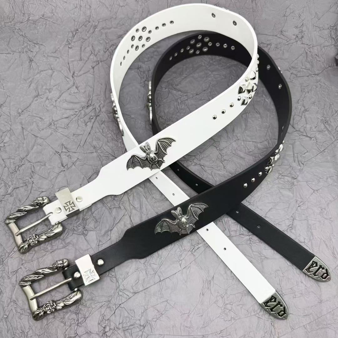 White and black bat emblem studded leather belts with ornate silver buckles on textured background.