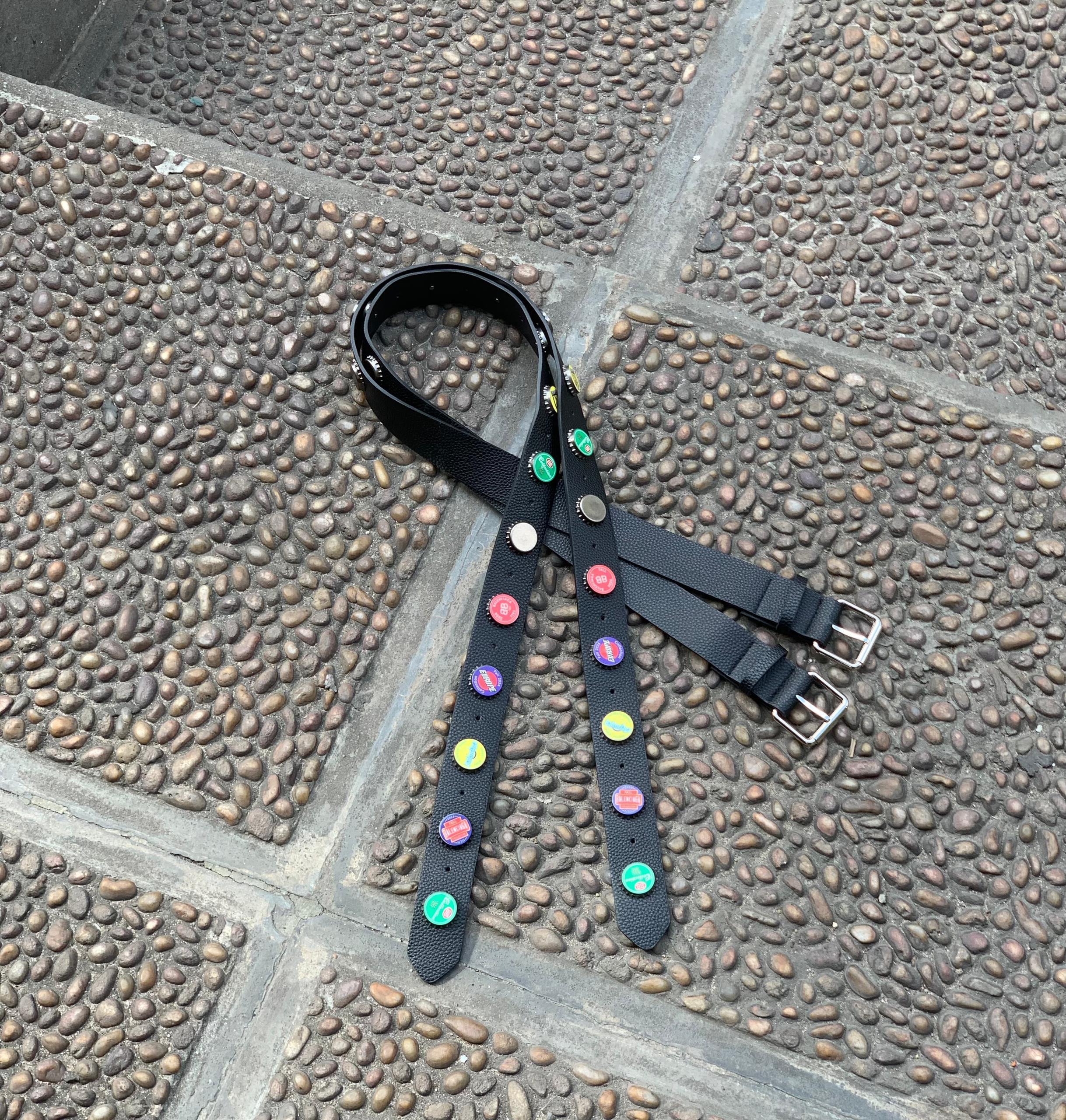 Black belt with multicolored bottle cap decorations and silver buckles laid on cobblestone.