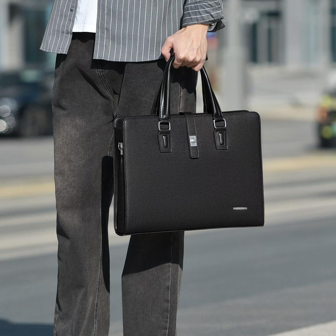 Man in striped shirt carrying a black textured laptop bag with dual handles and front clasp.
