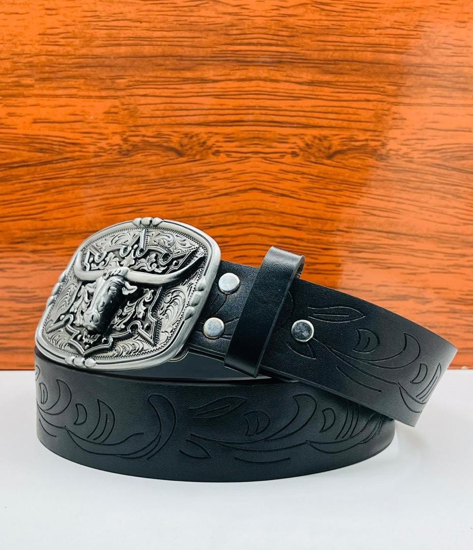 Black tooled leather belt with large silver bull head buckle on wood and white background.