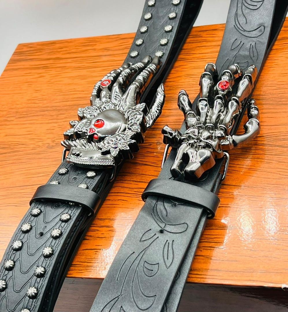 Two black leather belts with skeleton hand buckles and red details on wooden surface.