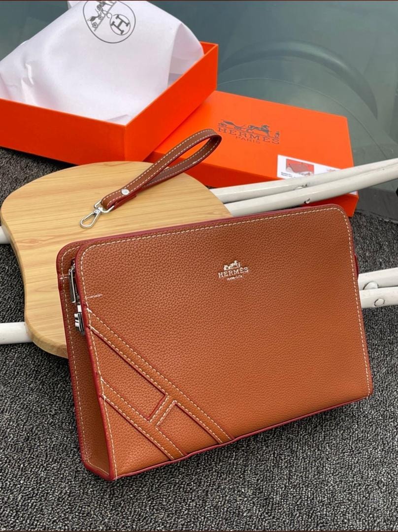 Brown Hermes purse with white stitching, logo detail and wrist strap with orange box.