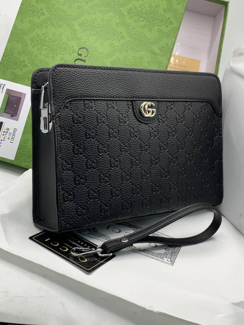 Black Gucci purse with GG monogram pattern, gold logo and wrist strap beside green box.