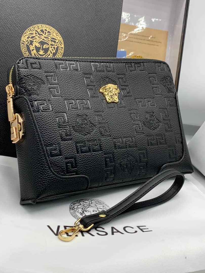 Black Versace purse with embossed Greek key pattern, Medusa logos, gold hardware and wrist strap.