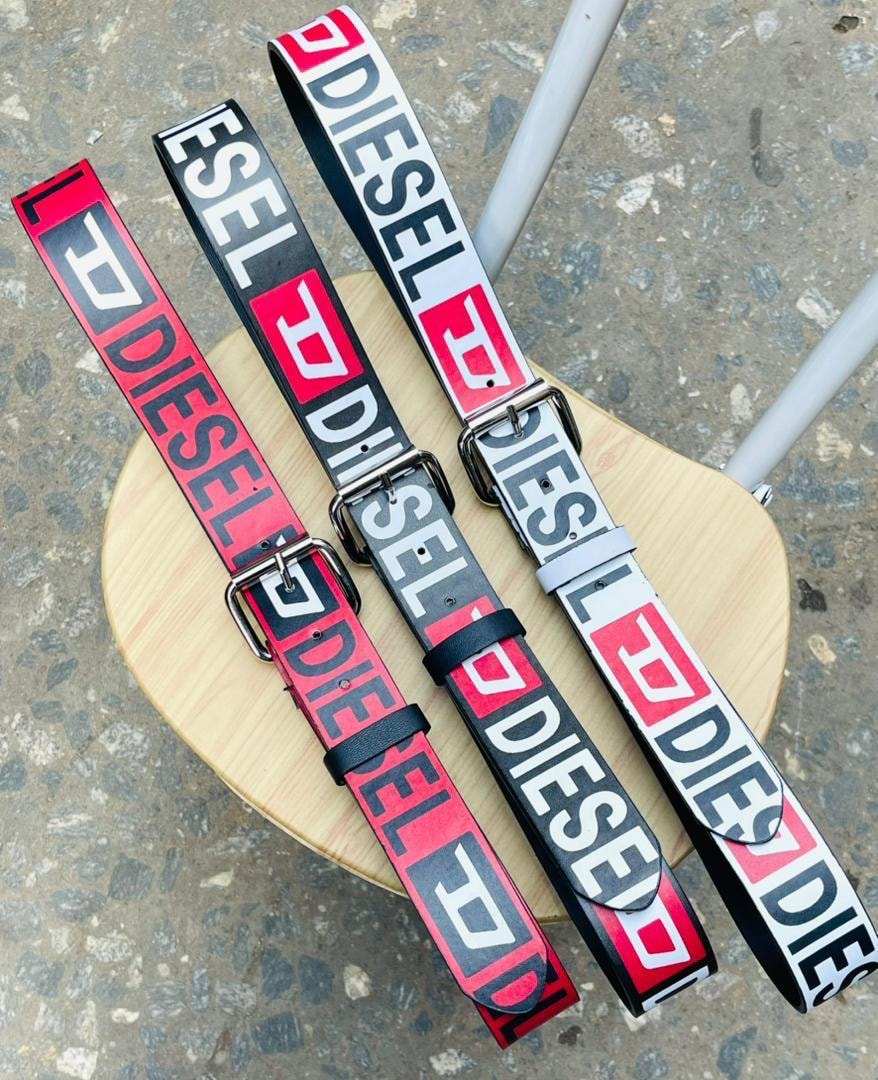 Three Diesel logo belts in red, black, and white laid out on a wooden stool.