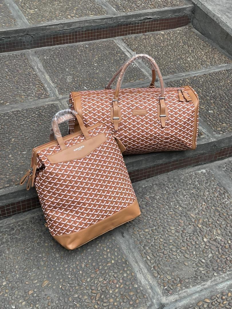 Brown Goyard pattern backpack and duffel bag set on stone steps.