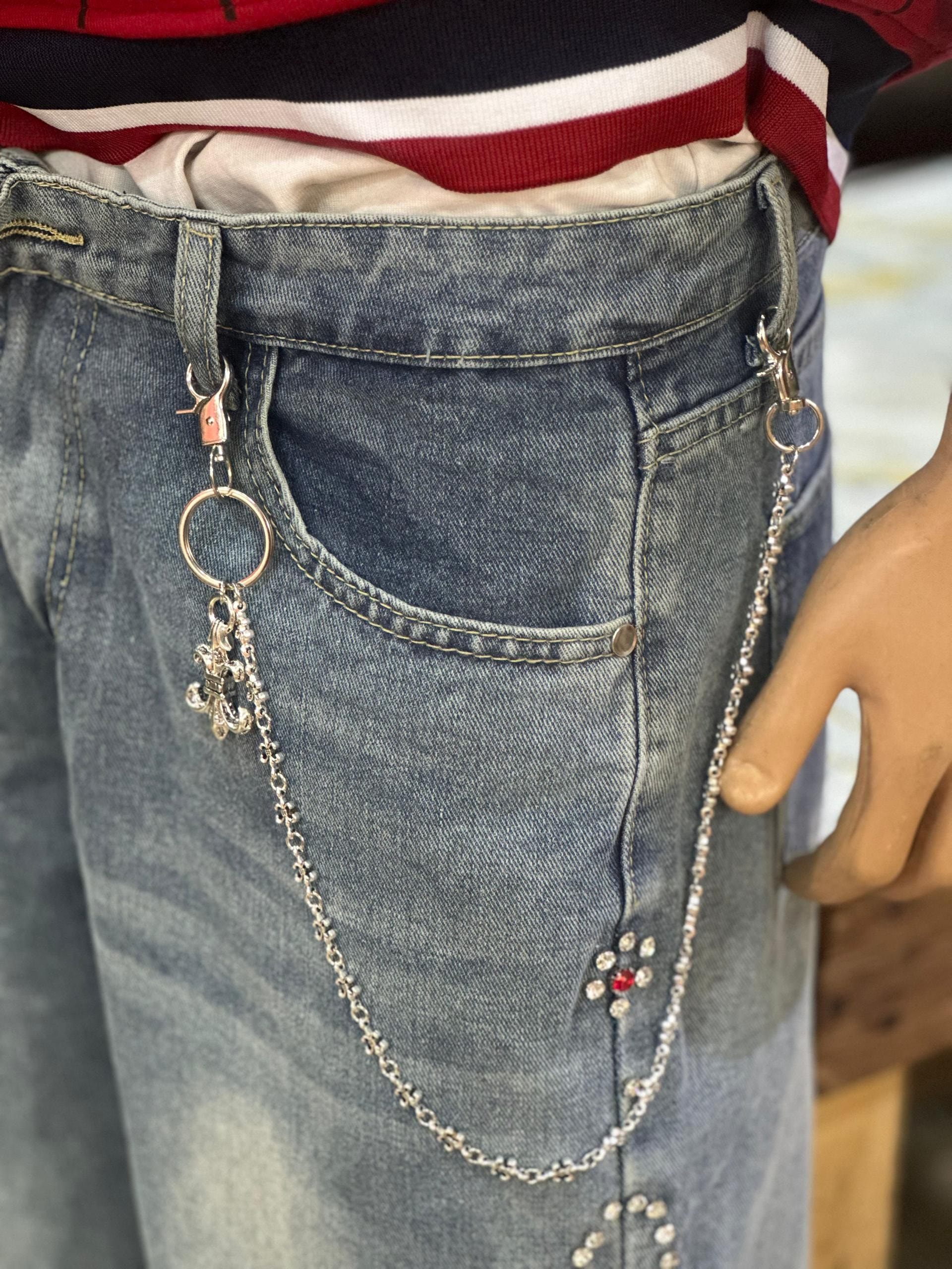 Silver jeans chain with decorative links and charm attached to light blue denim jeans on a mannequin.
