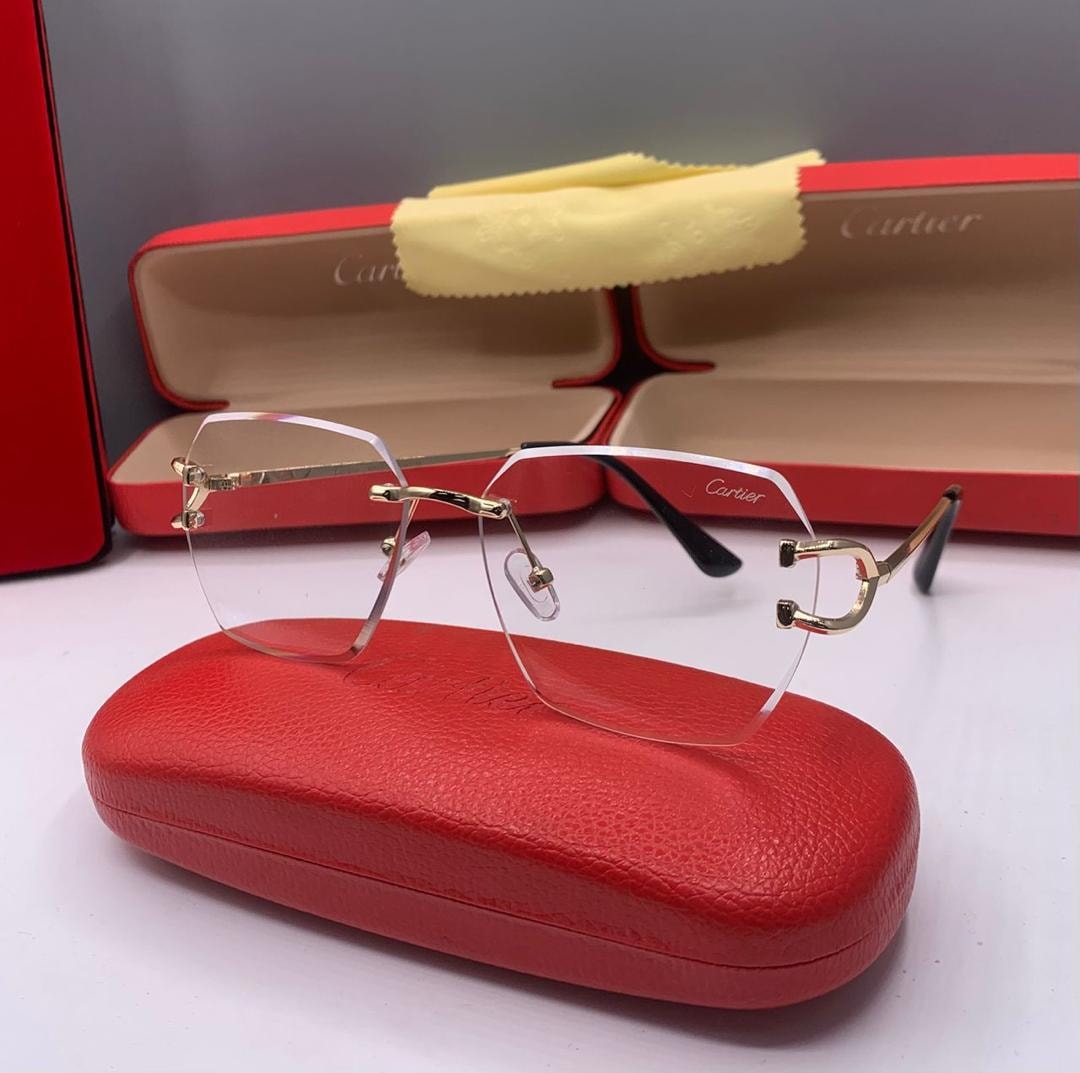 Cartier rimless clear eyeglasses with gold accents and red leather case in background.