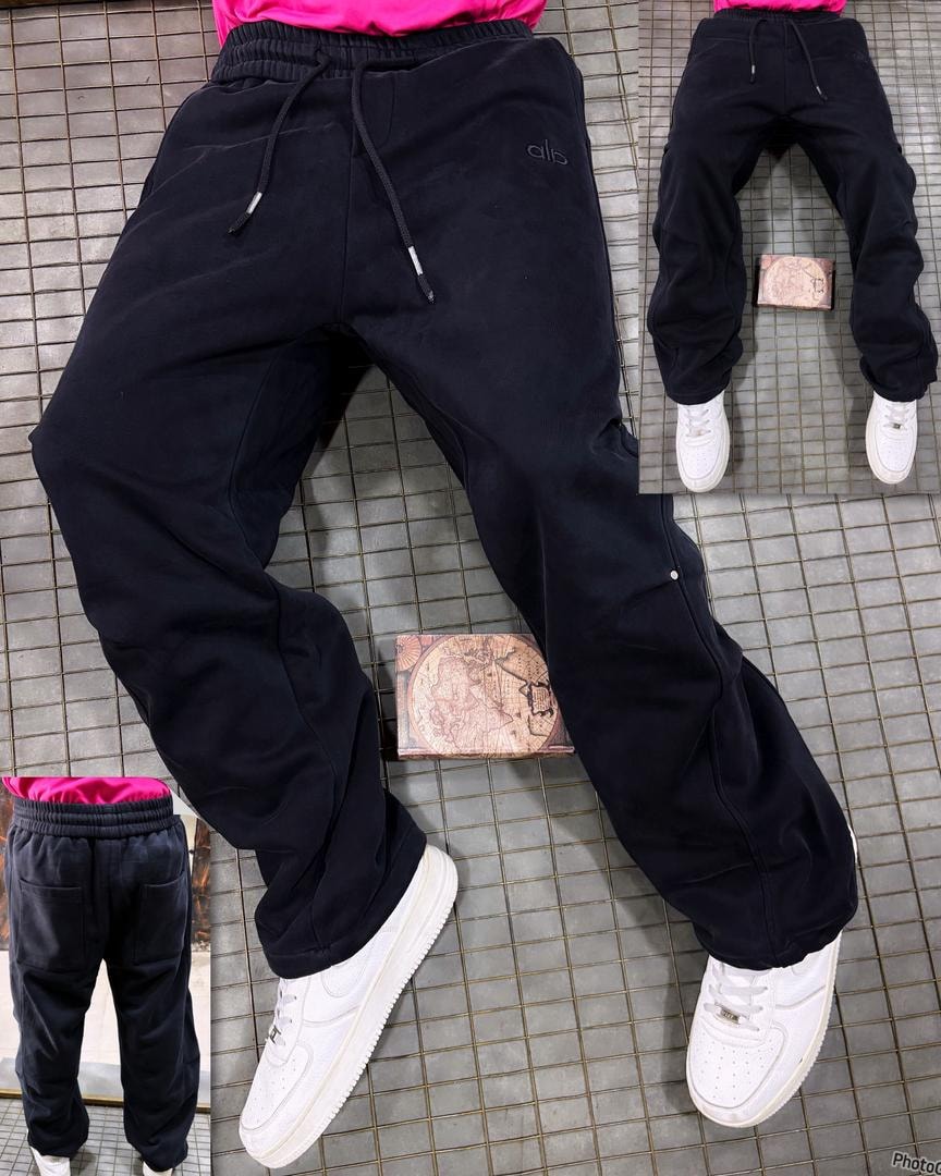 Model wearing plain black joggers with subtle embroidery, shown from front with white sneakers.