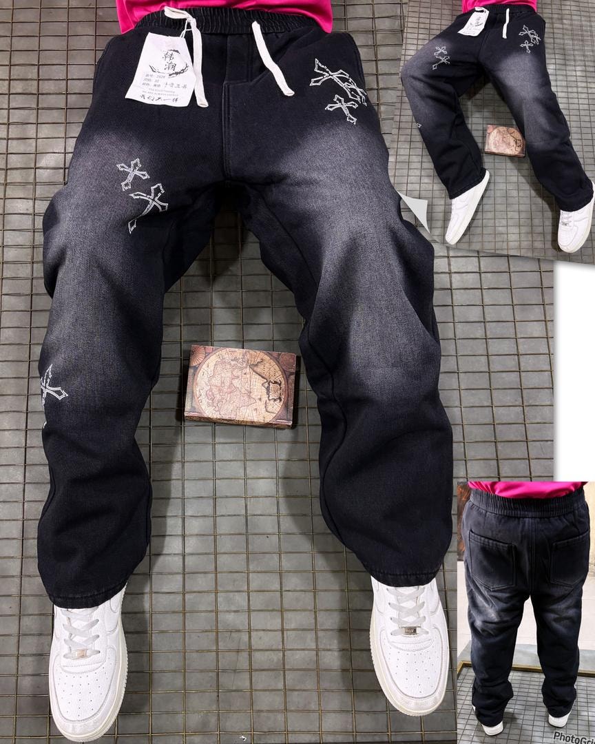 Model in black denim joggers with white cross embroidery patterns and white sneakers.