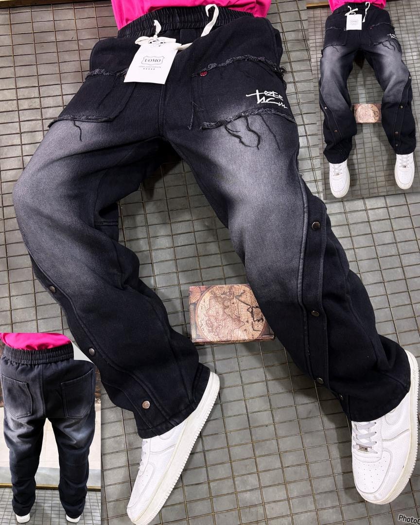Model wearing faded black denim joggers with script print, side buttons and white sneakers.