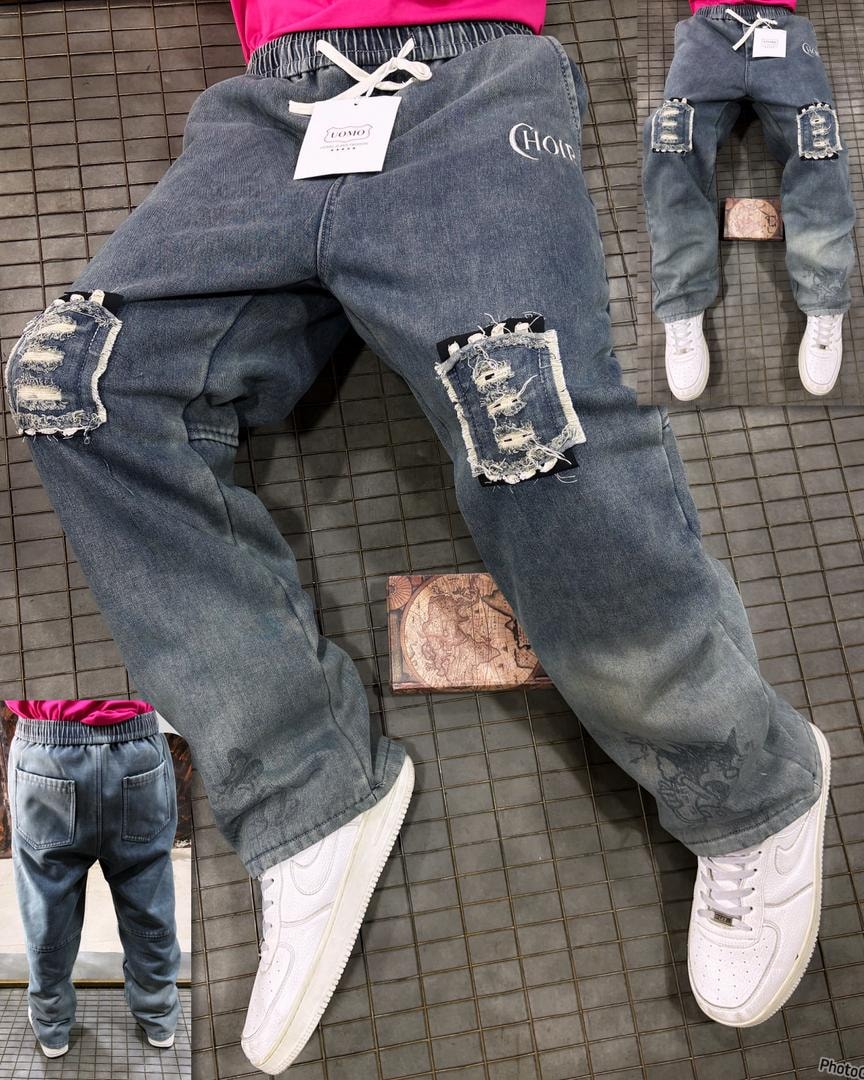 Model in blue denim graphic ripped joggers with CHOR embroidery and distressed knee patches.