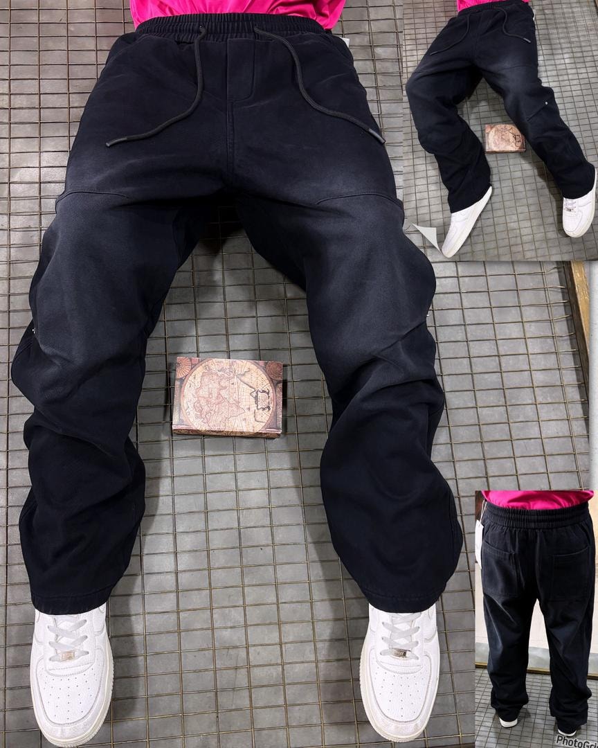 Rear view of model wearing plain black denim joggers with drawstring waist and white sneakers.