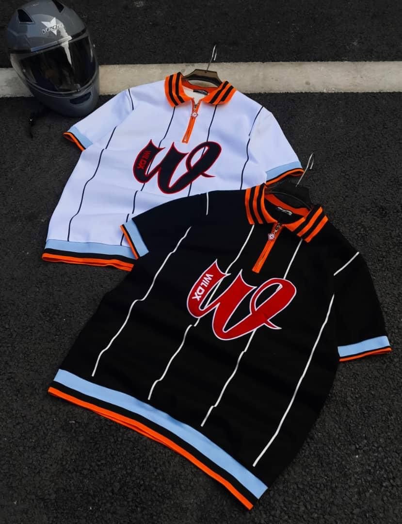 White and black WILD striped zip polo shirts laid on dark pavement.