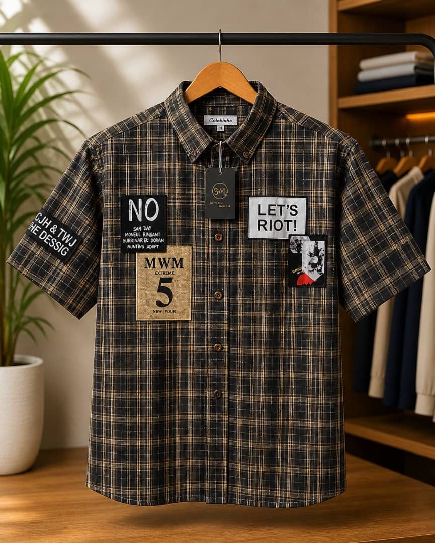 Dark plaid short sleeve collar shirt with multiple graphic patches on hanger.