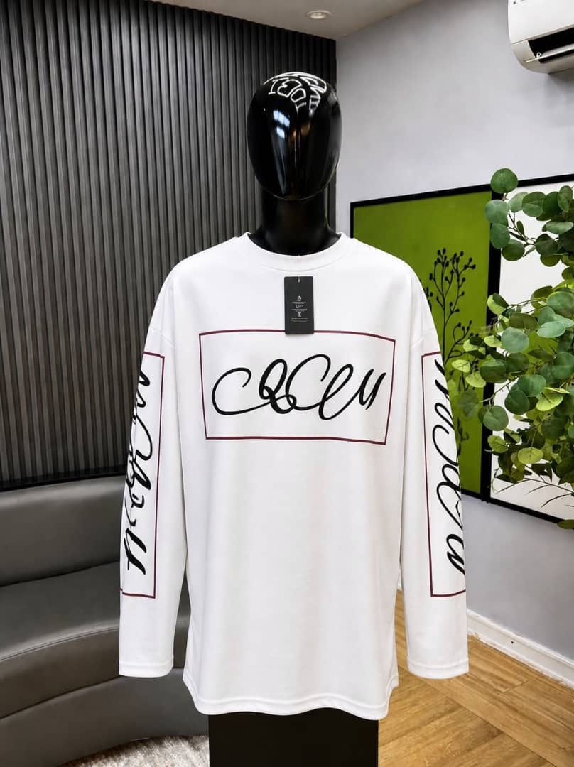 White long sleeve top with maroon-bordered cursive graphic on chest and sleeves on mannequin.