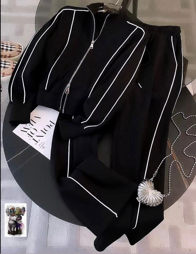 Black zip-up jacket and pants with white piping displayed on a round table with accessories.
