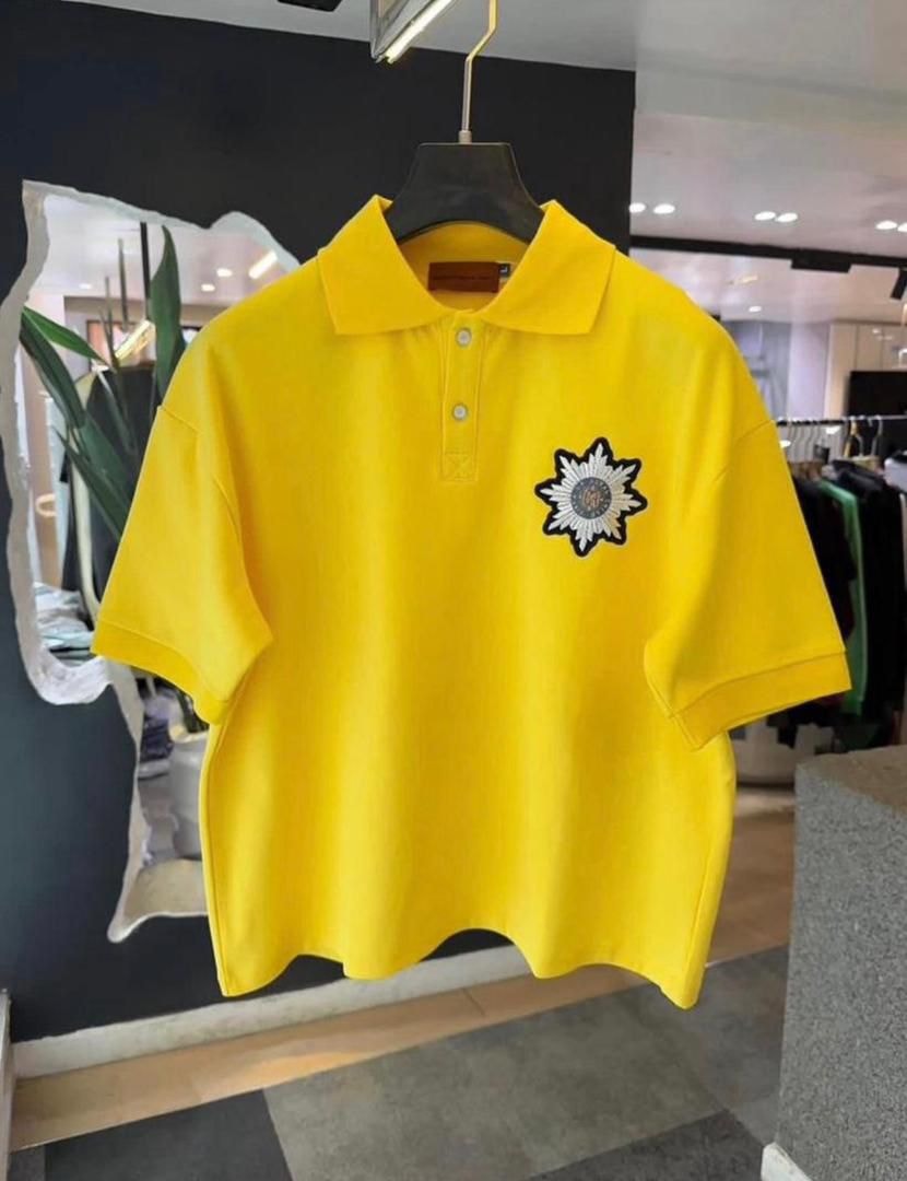 Bright yellow polo shirt with decorative embroidery hanging on display.