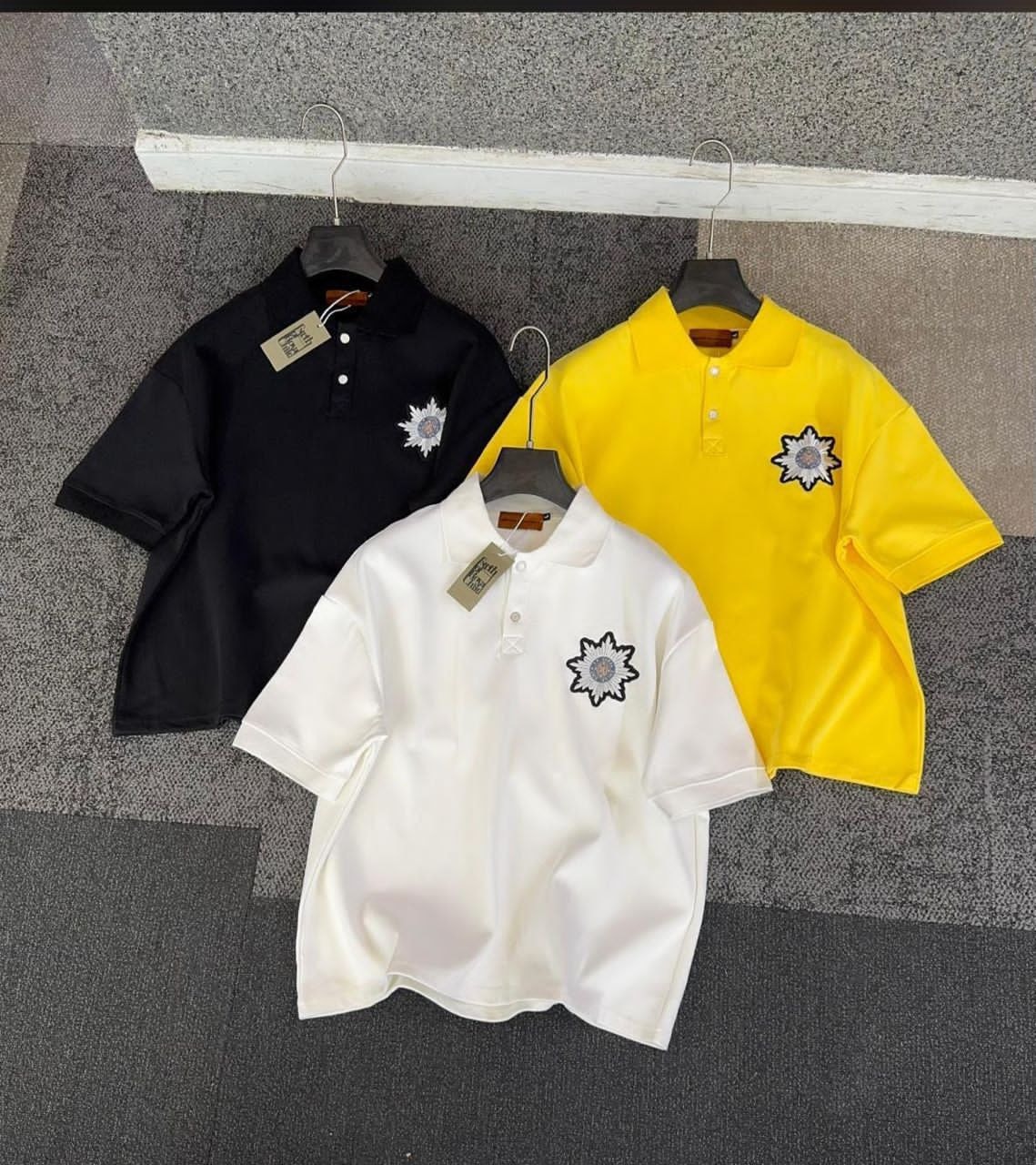 Three embroidered polo shirts in black, white, and yellow colors displayed together.