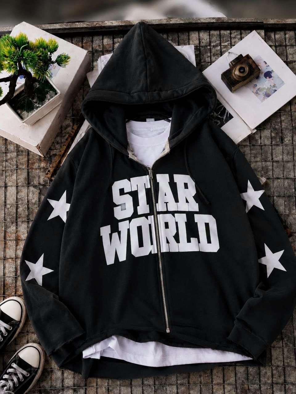 Black zip-up hoodie with STAR WORLD text and white stars on sleeves in flat lay.