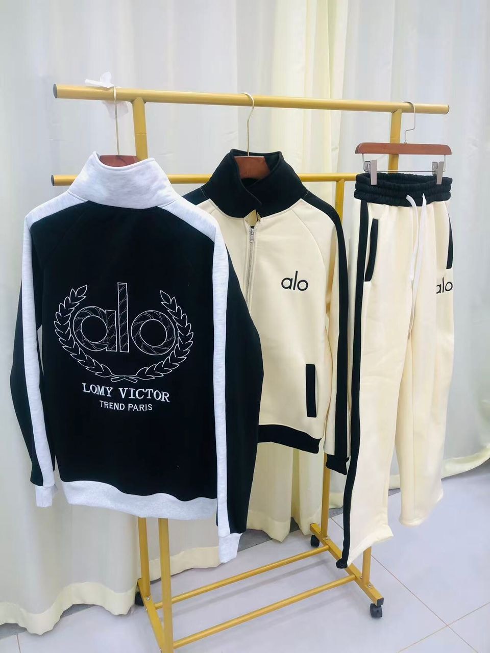 Black and cream alo two-piece tracksuits with contrast panels shown on a yellow rack.