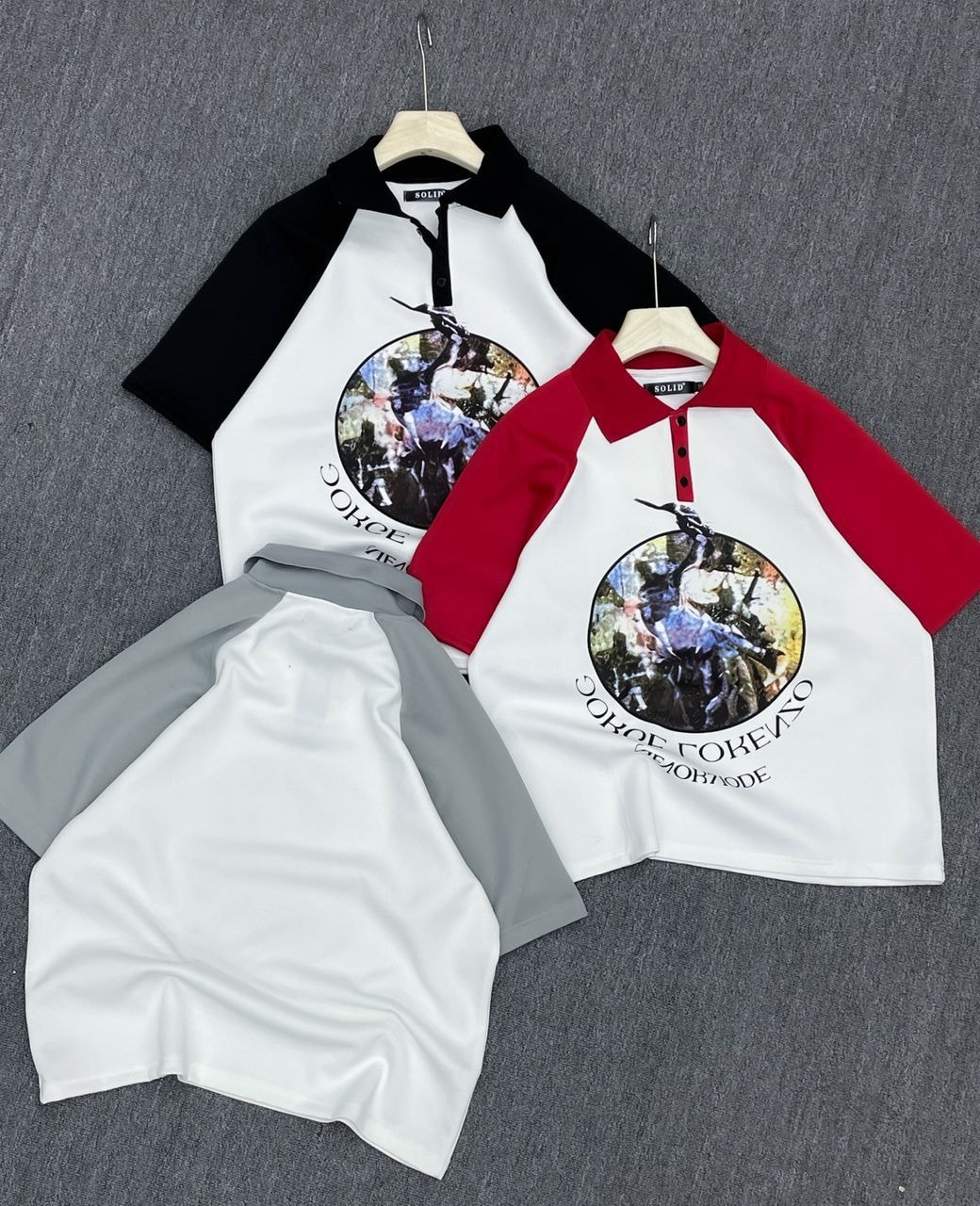 Two raglan polo shirts with circular graphic prints shown side by side, one with black sleeves and one with red sleeves, alongside white and grey shorts.