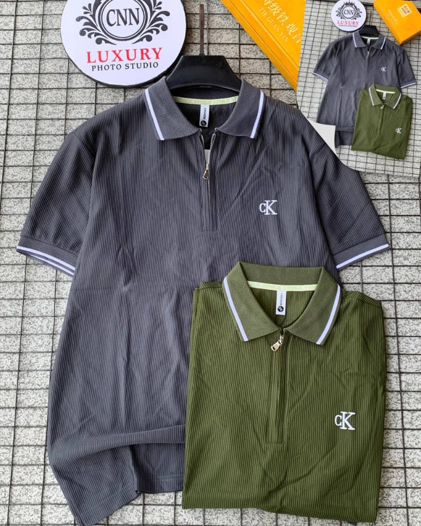 Gray and olive green CK ribbed zip collar polos laid flat on tiled floor with studio backdrop.