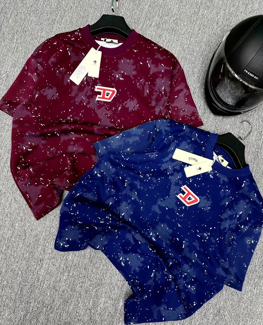 Burgundy and blue splatter t-shirts with red chest logo laid out next to black helmet.