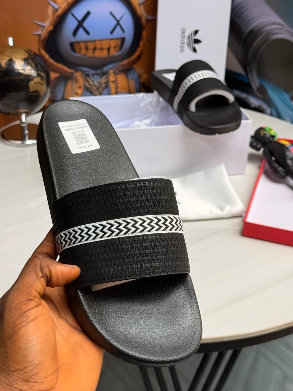 Black Adidas slides with woven textured strap and white pattern detail.