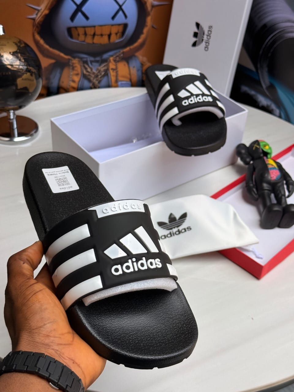 Black Adidas slides with white stripes and adidas logo on the strap.