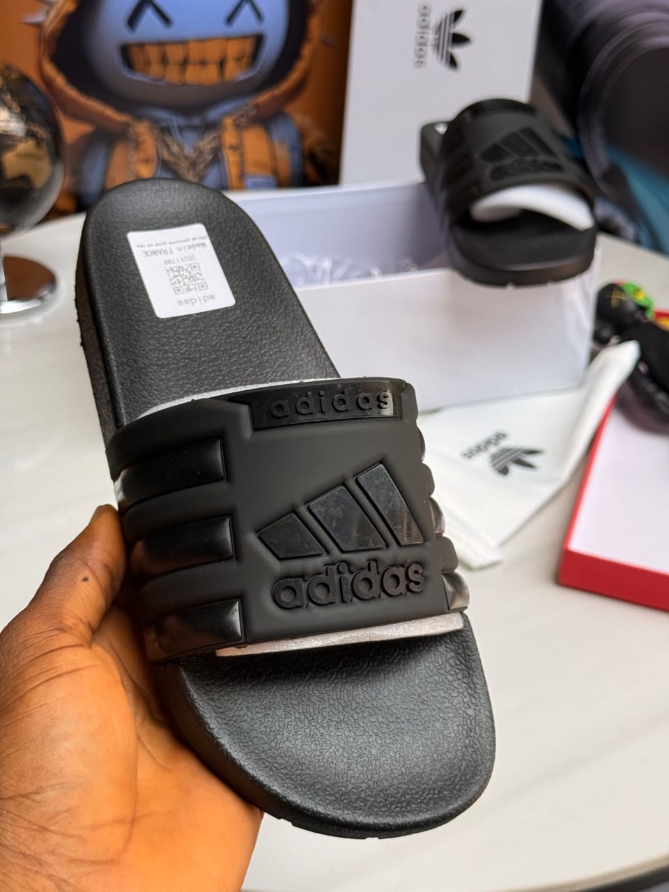 Black Adidas slides with raised logo and three stripe design on strap.