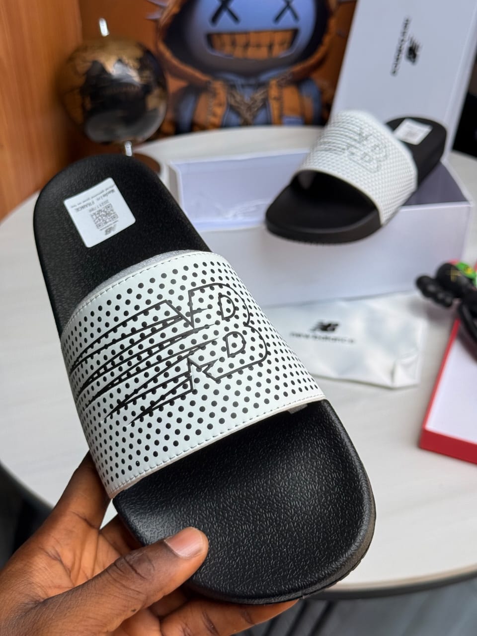 White and black New Balance slides with perforated pattern and NB logo.