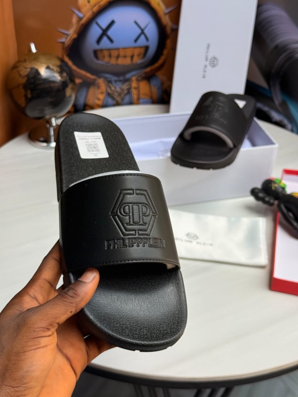 Hand holding black Philipp Plein slide with hexagon logo and text.